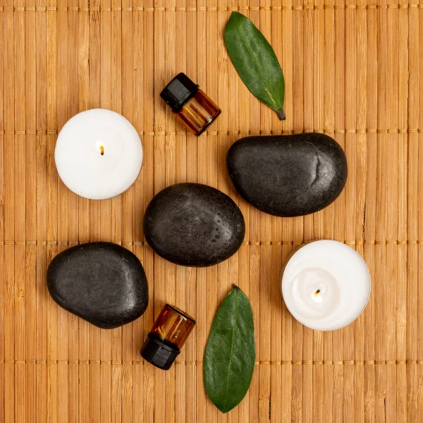 Pierres de spa et huiles essentielles disposées sur un tapis en bambou, évoquant un massage aux pierres chaudes.