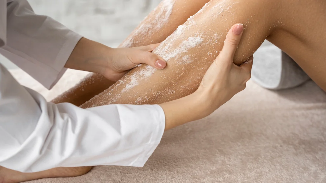 Une femme se rase les jambes avec un rasoir, utilisant un exfoliant pour le corps.