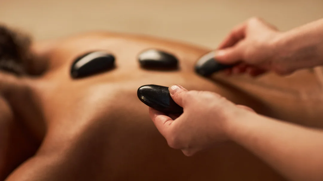 Femme recevant un massage aux pierres chaudes, allongée sur une table de massage, entourée d'une ambiance relaxante.