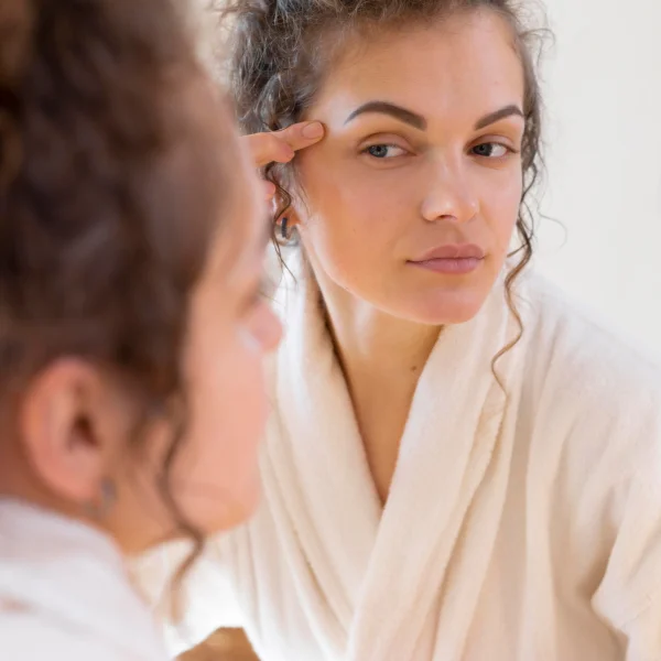 Une femme se regarde dans le miroir en appliquant son maquillage après une séance de microdermabrasion du visage.
